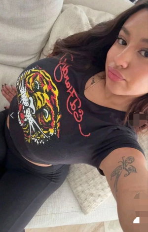 Woman with long dark hair in black t-shirt taking selfie on couch.