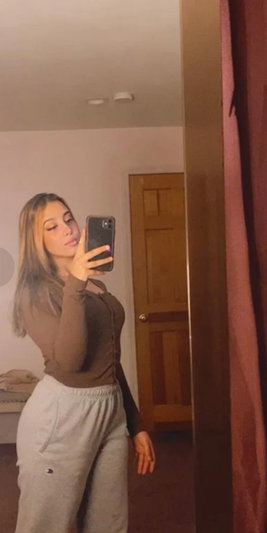 Woman with long blonde hair taking a mirror selfie in a bedroom.
