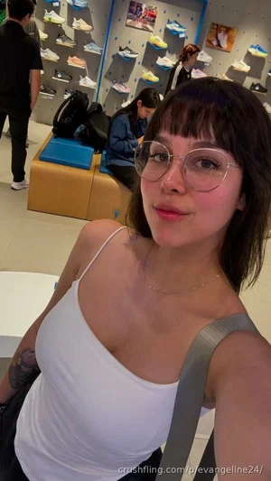 Woman with short dark hair and glasses wearing white tank top in shoe store.