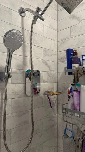Shower with marble tiles, handheld showerhead, and toiletries on racks.