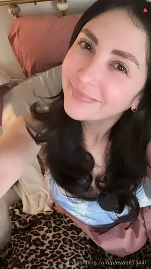 Woman with dark hair in a light blue top, lying in bed with leopard print and pink bedding.