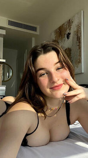 Brown-haired woman in black lingerie posing for a bedroom selfie.