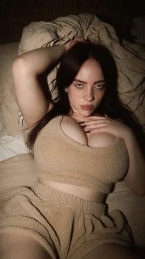 Woman with long dark hair in beige fuzzy top and shorts lying on bed.