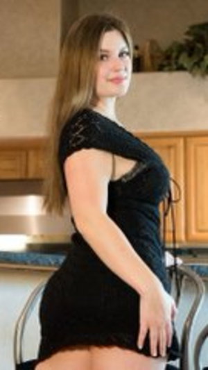 Woman in black lace dress posing in kitchen, curvy figure, long hair.