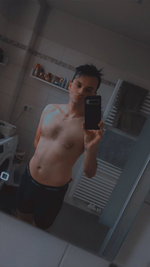 Man taking mirror selfie in bathroom wearing black shorts.