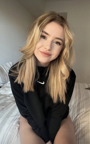 Blonde woman in black sweatshirt sitting on bed.