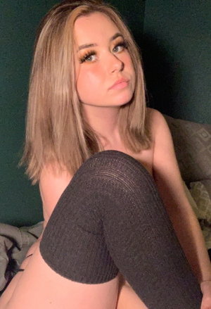 Blonde woman in dark stockings posing indoors on bed.