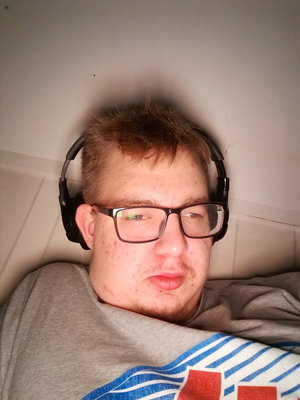 Man with glasses and headphones lying indoors in gray shirt.