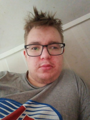 Young man with glasses wearing gray t-shirt indoors.