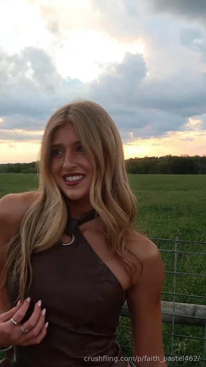 Woman with blonde hair in a brown halter top standing in a grassy field at sunset.