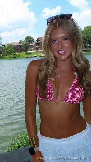 Woman in pink polka-dot bikini top and white skirt, smiling by a lake.