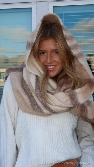 Woman with blonde hair wearing white ribbed sweater and striped scarf, smiling outdoors.