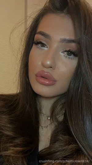 Woman with long brown hair and makeup, wearing a necklace, indoors.