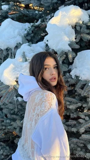 Woman in white lace hoodie poses in snowy pine trees outdoors.