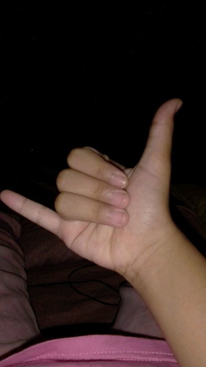 Hand making a rock gesture, pink fabric visible, dark background.
