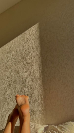 Bare feet on a bed with sunlight casting shadows on a textured wall.
