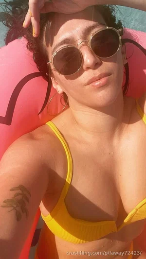 Woman in yellow bikini top on pink float, wearing sunglasses, outdoor setting.