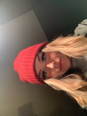 Woman with blonde hair wearing red beanie and gray top, indoors.