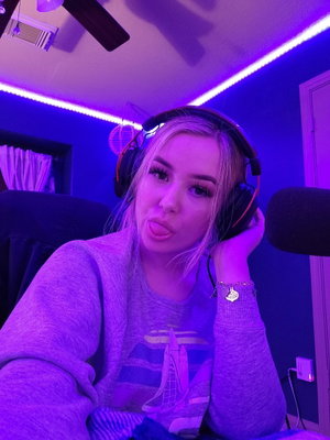Woman with blonde hair wearing headphones and a gray sweatshirt in a room with purple LED lights.