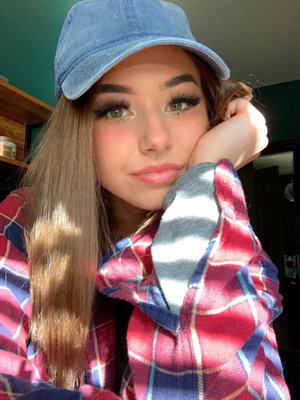 Woman with long hair wearing plaid shirt and blue cap, posing indoors.