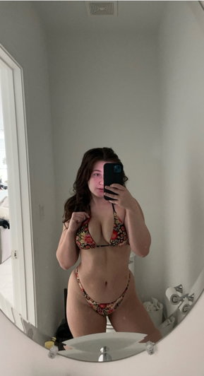 Woman in floral bikini taking mirror selfie in bathroom.