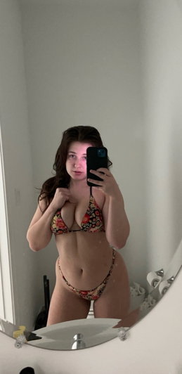 Woman in floral bikini taking mirror selfie in bathroom.