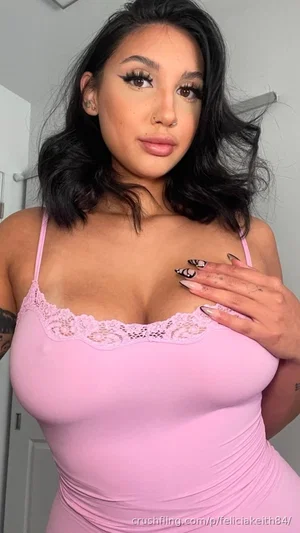 Woman with dark hair in pink lace lingerie, indoors, hand on chest.