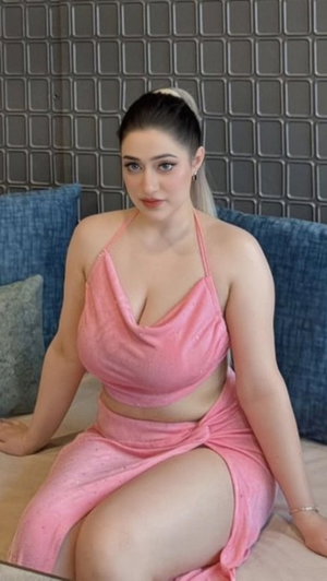 Woman in pink two-piece outfit sitting on bed with blue pillows and textured wall behind.