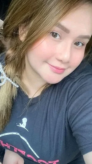 Woman with light brown hair in a dark t-shirt, smiling in a close-up selfie.