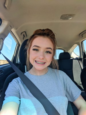 Woman with braces and long hair in a gray t-shirt, smiling in a car.