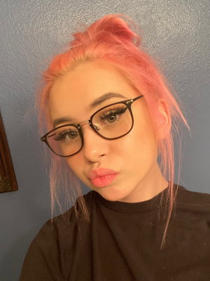 Woman with pink hair and glasses in a black top, indoors.