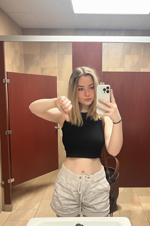 Blonde woman taking mirror selfie in bathroom wearing black top and shorts