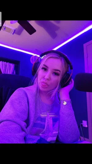Woman with blonde hair wearing headphones and a gray sweatshirt in a room with purple lighting.