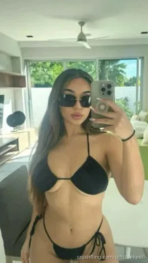 Woman in black bikini taking mirror selfie in bright indoor space.