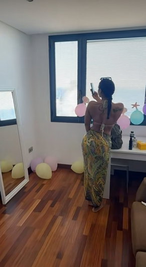 Woman with dark hair in bikini top and patterned skirt indoors.
