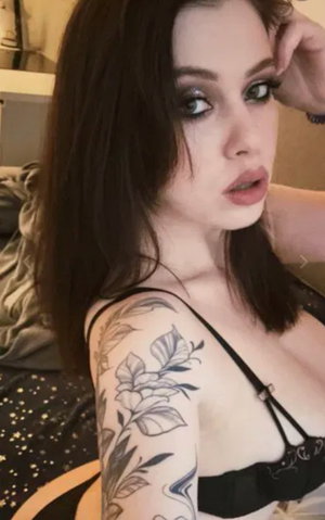Dark-haired woman with floral tattoos wearing black bra indoors.