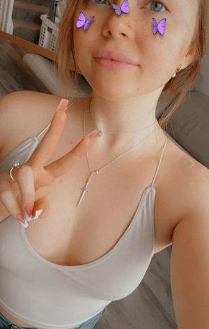 Freckled woman in white tank top taking indoor selfie.