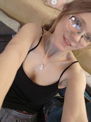 Woman with glasses in black tank top taking bedroom selfie.