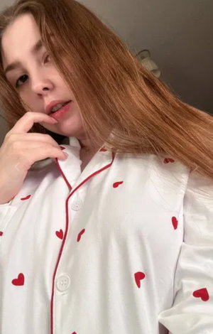 Woman with long auburn hair in heart pajamas indoors.
