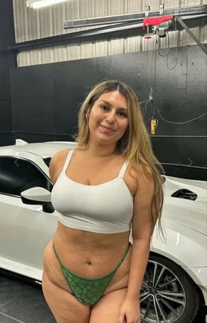Curvy woman in white crop top and green panties in garage.