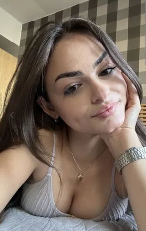 Woman with long brown hair in gray top posing indoors.