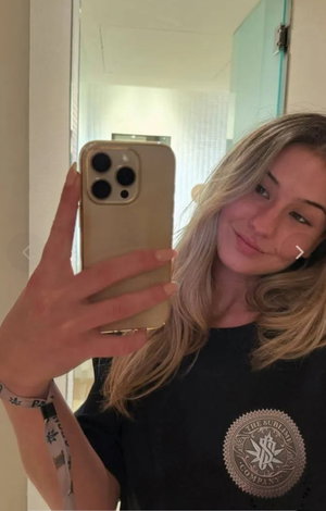 Blonde woman taking mirror selfie in black t-shirt indoors.