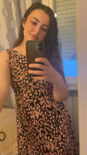 Woman with dark hair in floral dress taking mirror selfie indoors.