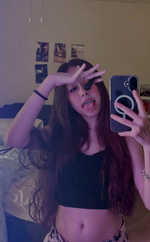 Woman with long brown hair in black crop top taking mirror selfie.