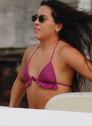 Curvy woman in pink bikini and sunglasses with windblown hair outdoors.
