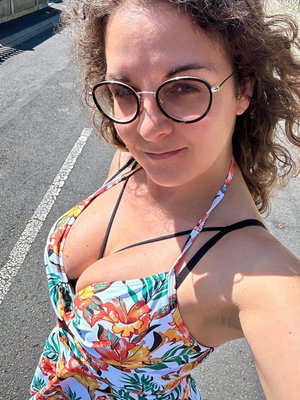Curly-haired woman in floral top taking outdoor selfie.