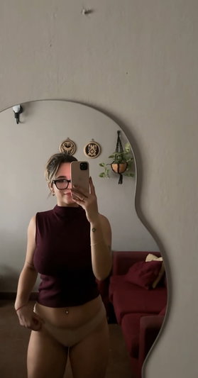 Woman in maroon top and beige underwear takes mirror selfie in bedroom.