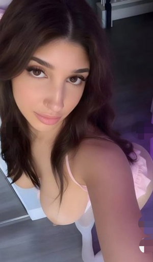 Woman with long brown hair in pink lingerie taking selfie indoors.