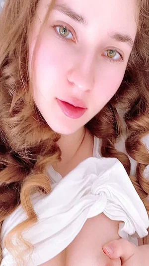 Woman with curly brown hair in white top taking selfie.