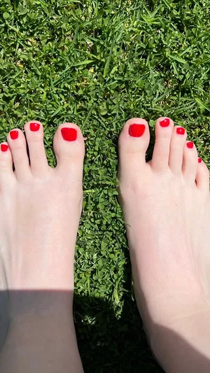 Bare feet with red toenail polish on green grass.